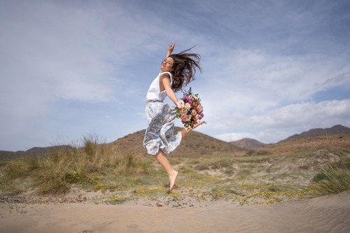 donna in mezzo a una valle che salta con mazzo di fiori in mano