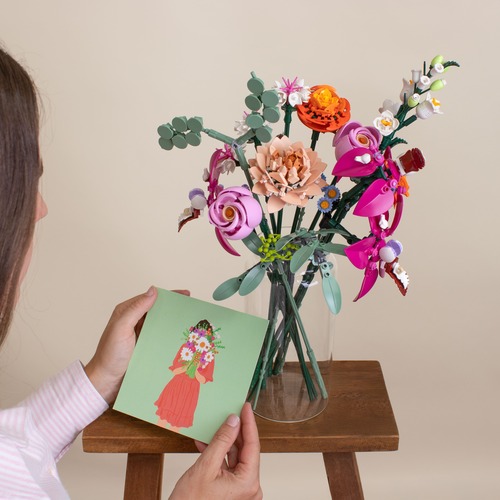Ragazza che tiene in mano un biglietto di auguri e sullo sfondo vaso con fiori Lego colorati
